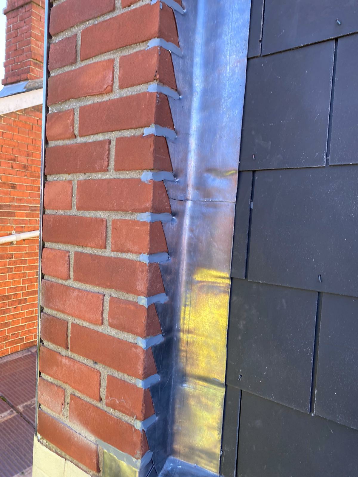 New lead step flashing against a brick wall on a slate roof