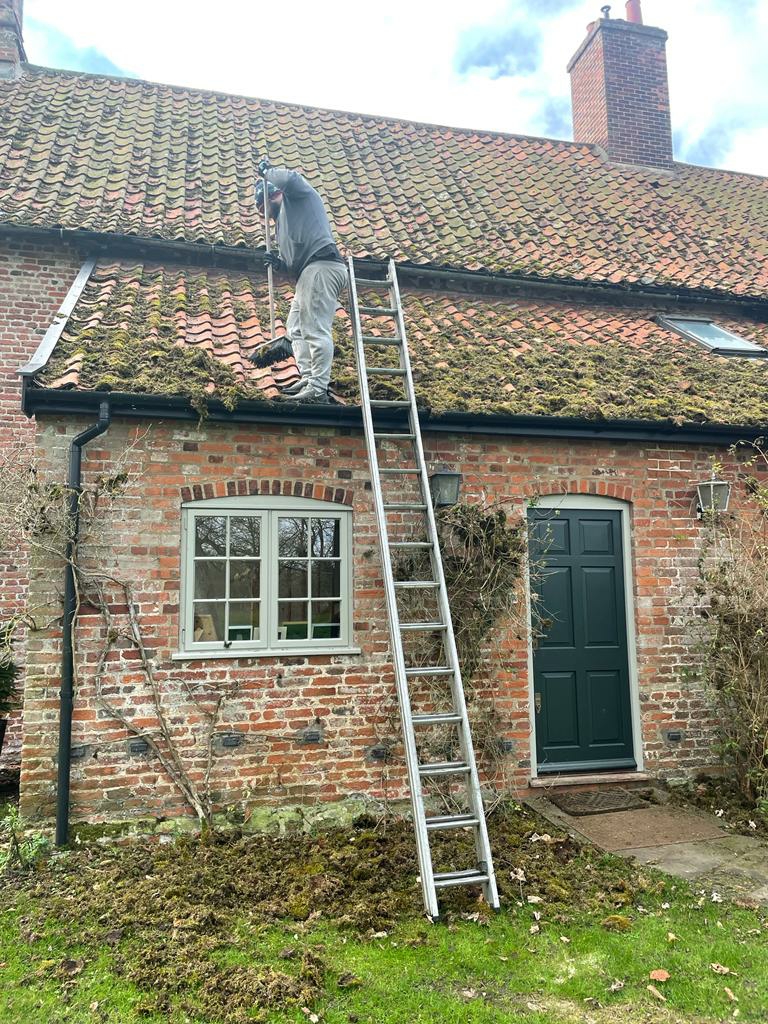 Roofer on a ladder working on a mossy pantile cottage roof
