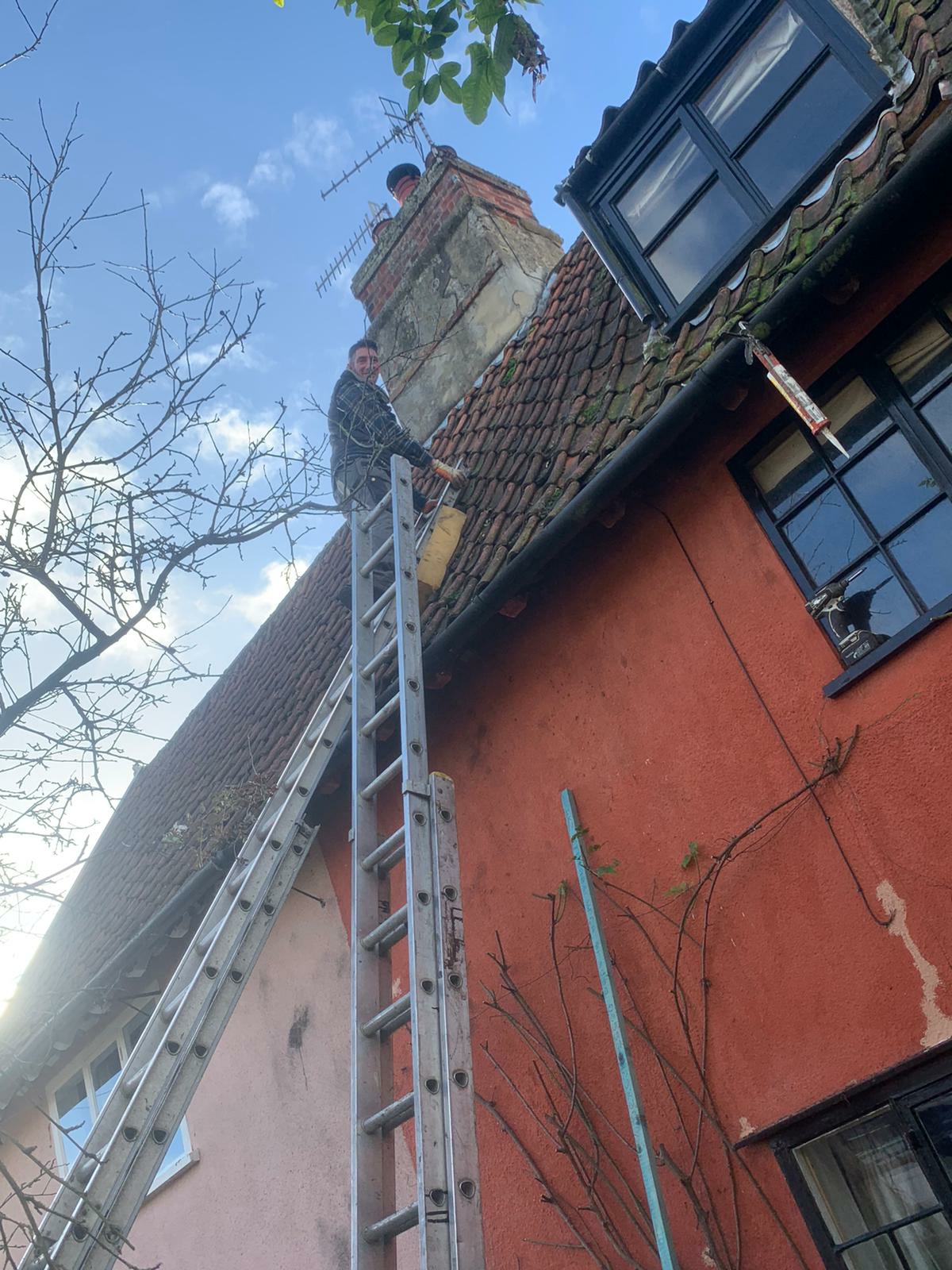Roofer on ladders at a pink-washed Suffolk cottage