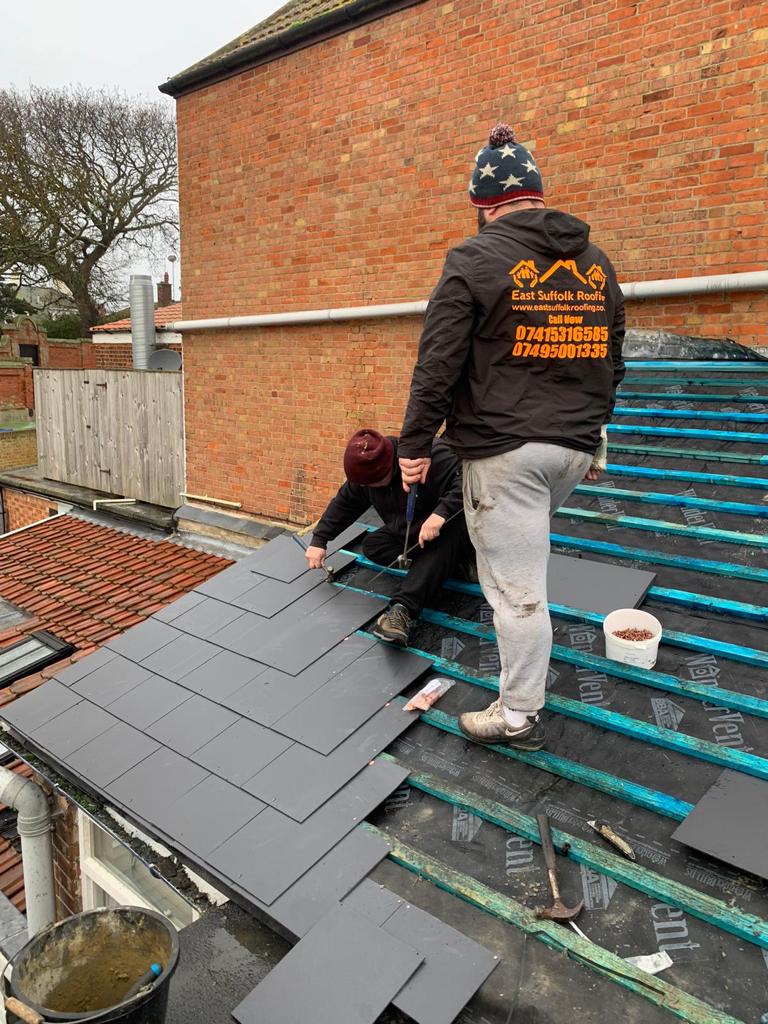 Two roofers laying new slates over fresh battens